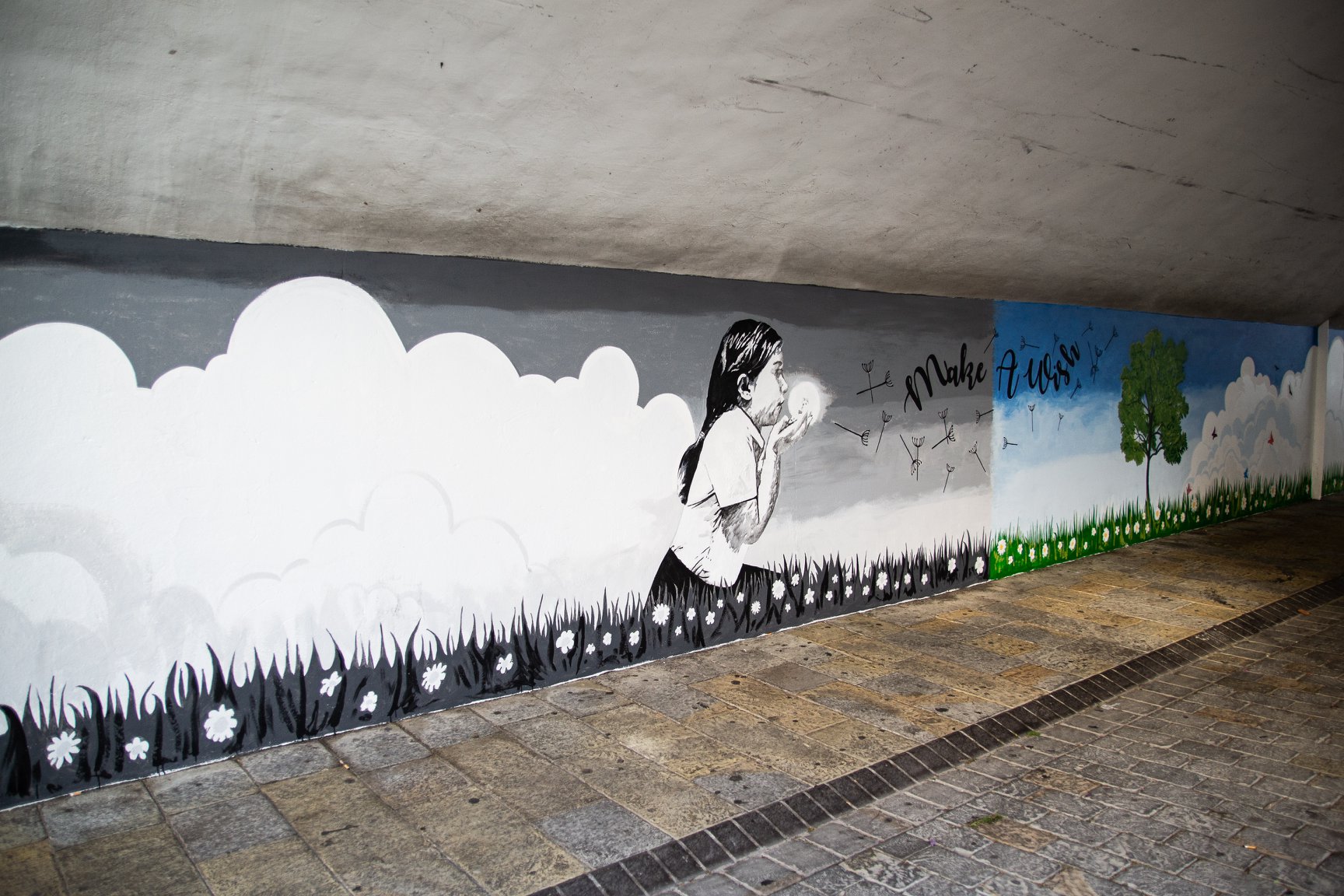 <h2>Street Art Project Gibraltar (Chatham Counterguard / Irish Town Tunnel)</h2>

In December 2017, the Gibraltar Government opened a competition to the public to come up with original street art designs. </br></br>

Aside from my graphic design career, I am also an artist. I entered the competition and was successful, being awarded the location at Chatham Counterguard tunnel by Irish Town in Gibraltar.</br></br>

In this day and age, gone are the wide open spaces of Gibraltar, and the heritage buildings struggle to compete with the monstrosities of modern contemporary architecture.</br></br>

The pollution we are exposed to is so harsh here; I feel that there should be more green spaces to help with cleaner air.</br></br>

‘Make a Wish’ invites the viewer to leave behind the hustle and bustle of modern life and walk into nature’s paradise. Part of the murals are black and white representing pollution and then you walk into a kaleidoscope of colour. The child (in a style not dissimilar to Banksy) transforms the mural into colour, but at the same time, invites the passer-by to make a wish. So often we see people engrossed in their mobile phones as they walk that they forget the beauty around them.
